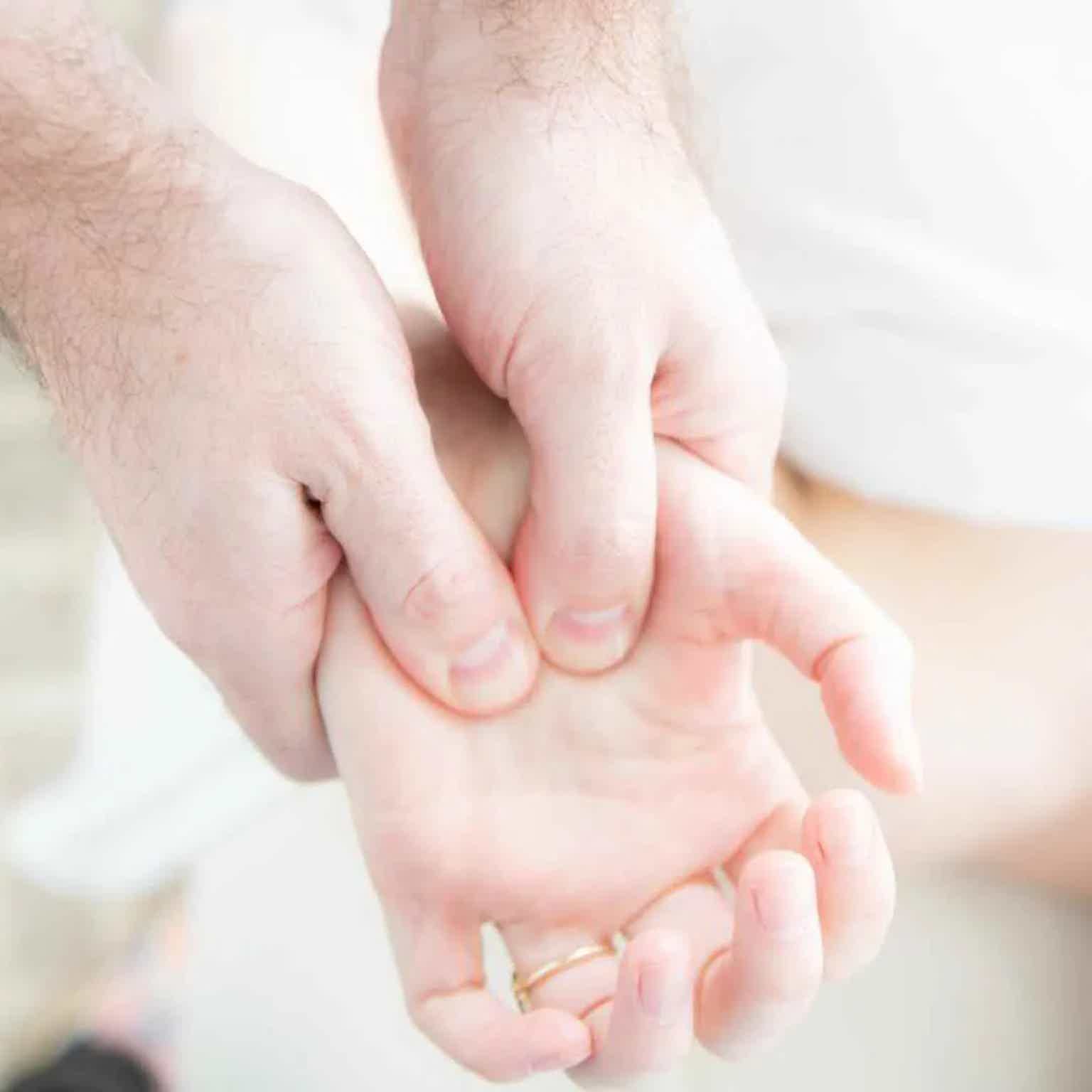 Two adult hands gently holding and supporting a small finger, close-up on light skin tones.