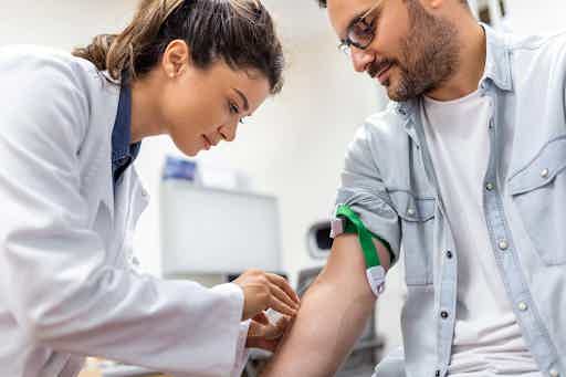 A clinician in a white lab coat drawing a venous blood sample from a patient's arm for IgG food sensitivity testing.