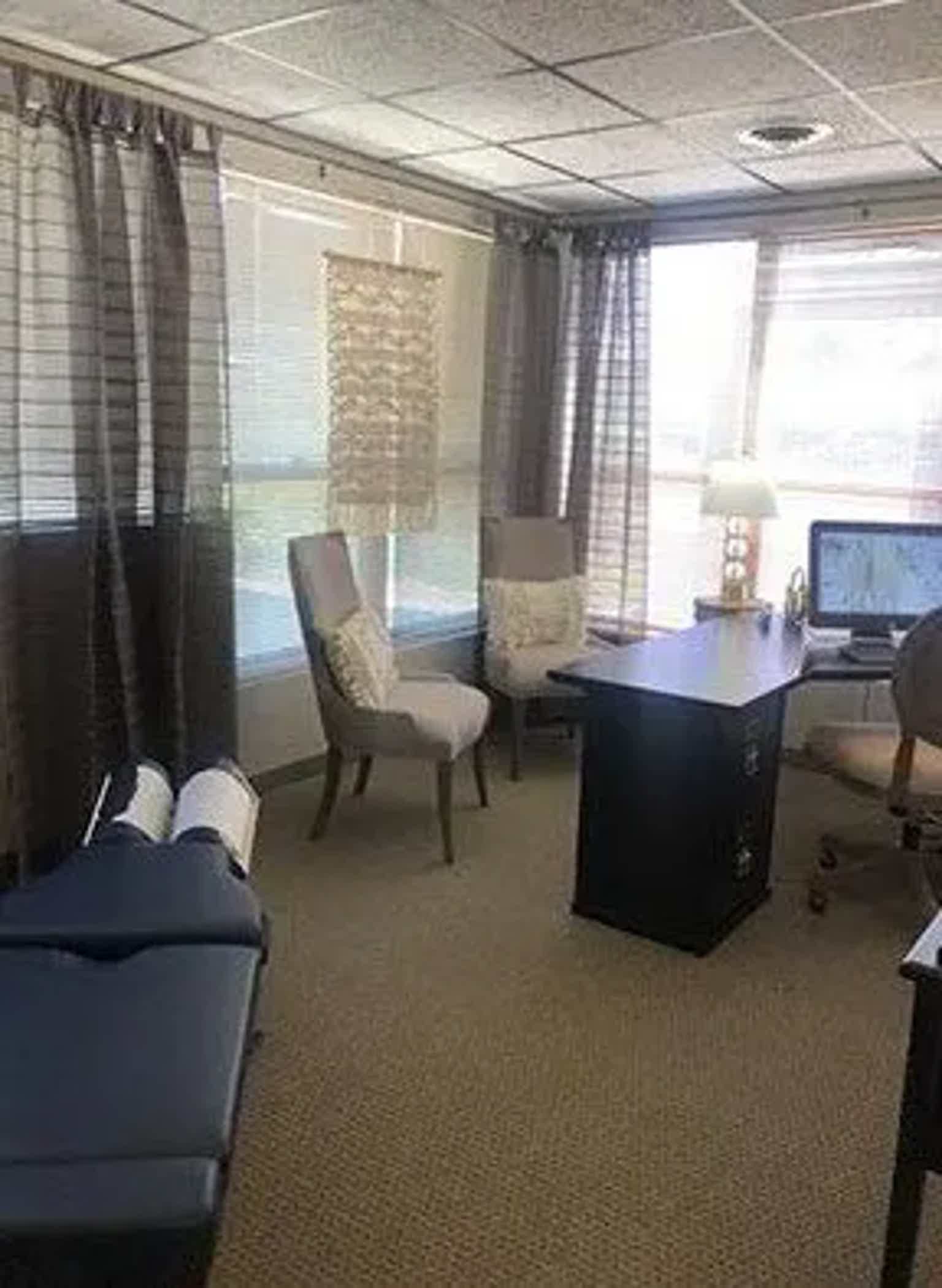 Office meeting room with chairs, desk, computer, and large windows behind dark curtains.