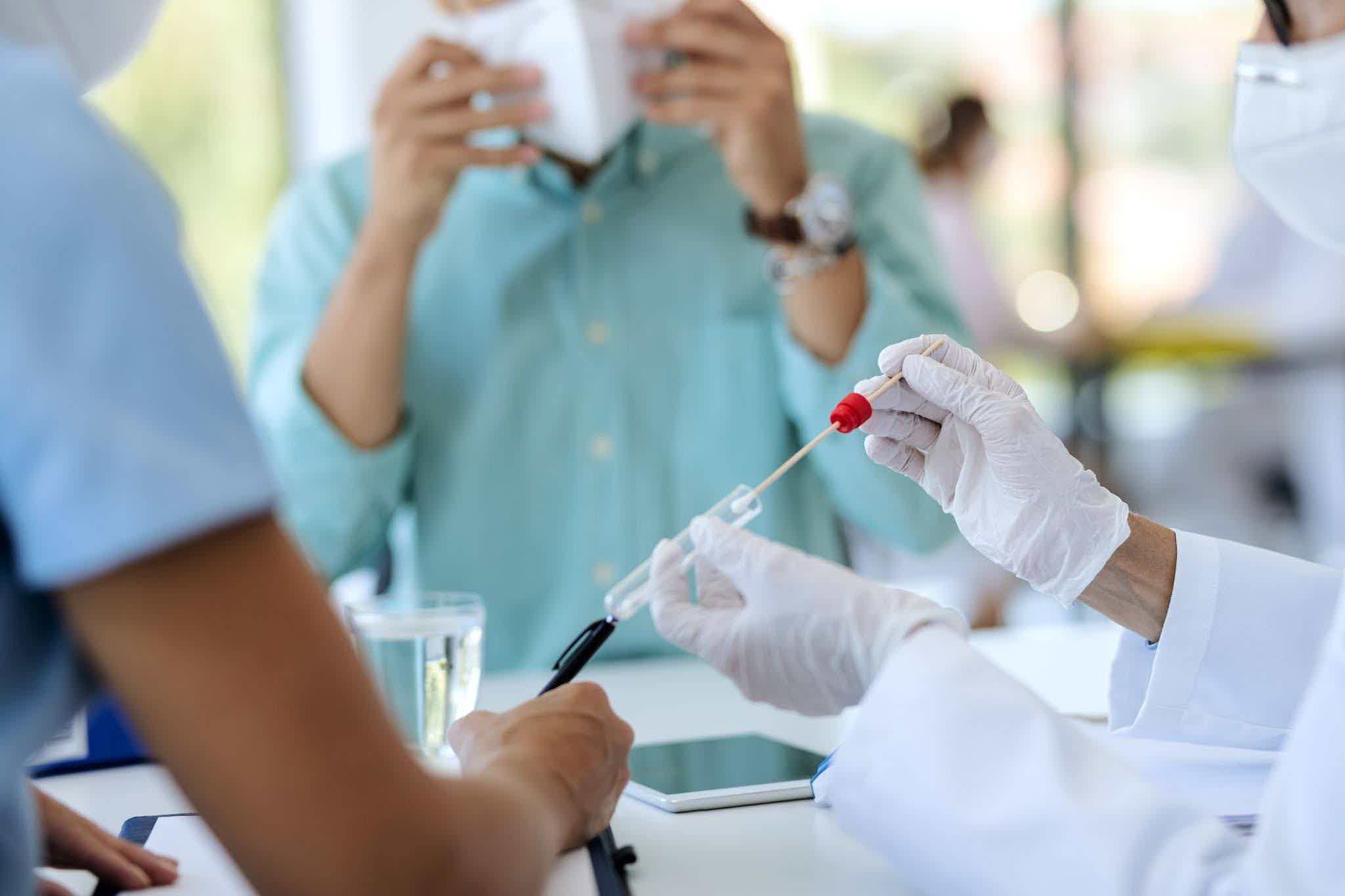 Gloved healthcare worker collecting a sample with a swab and placing it into a test tube at a clinic.