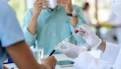 Gloved healthcare worker collecting a sample with a swab and placing it into a test tube at a clinic.