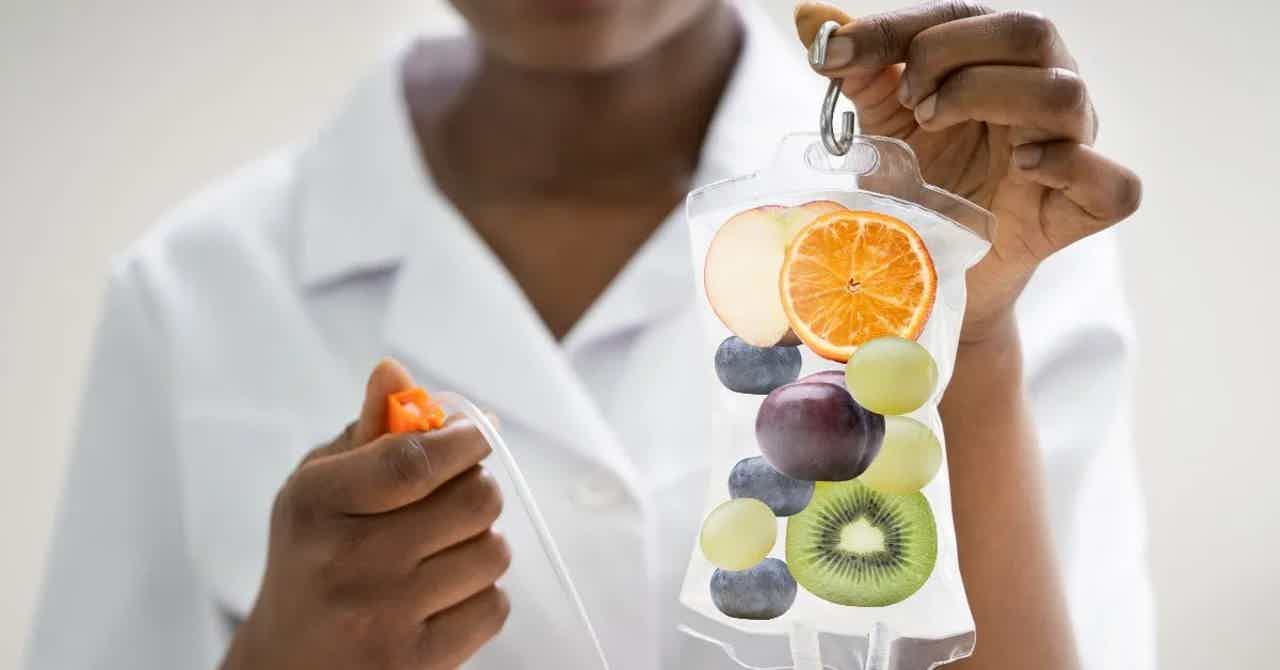 Medical professional holding a hanging pouch of assorted fruits, sliced orange top, with syringe in other hand.