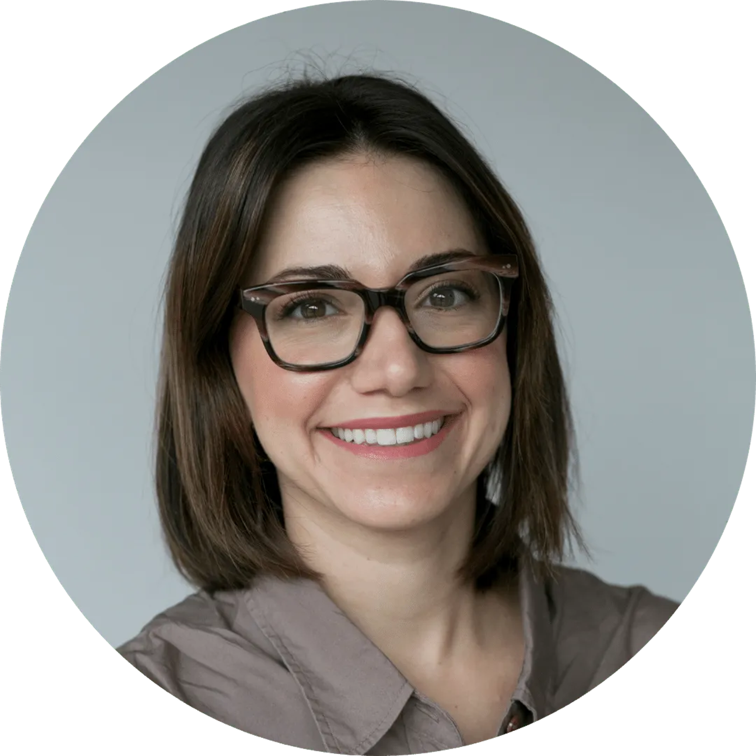 Smiling woman with dark brown shoulder-length hair wearing black rectangular glasses, studio portrait against light backgroun