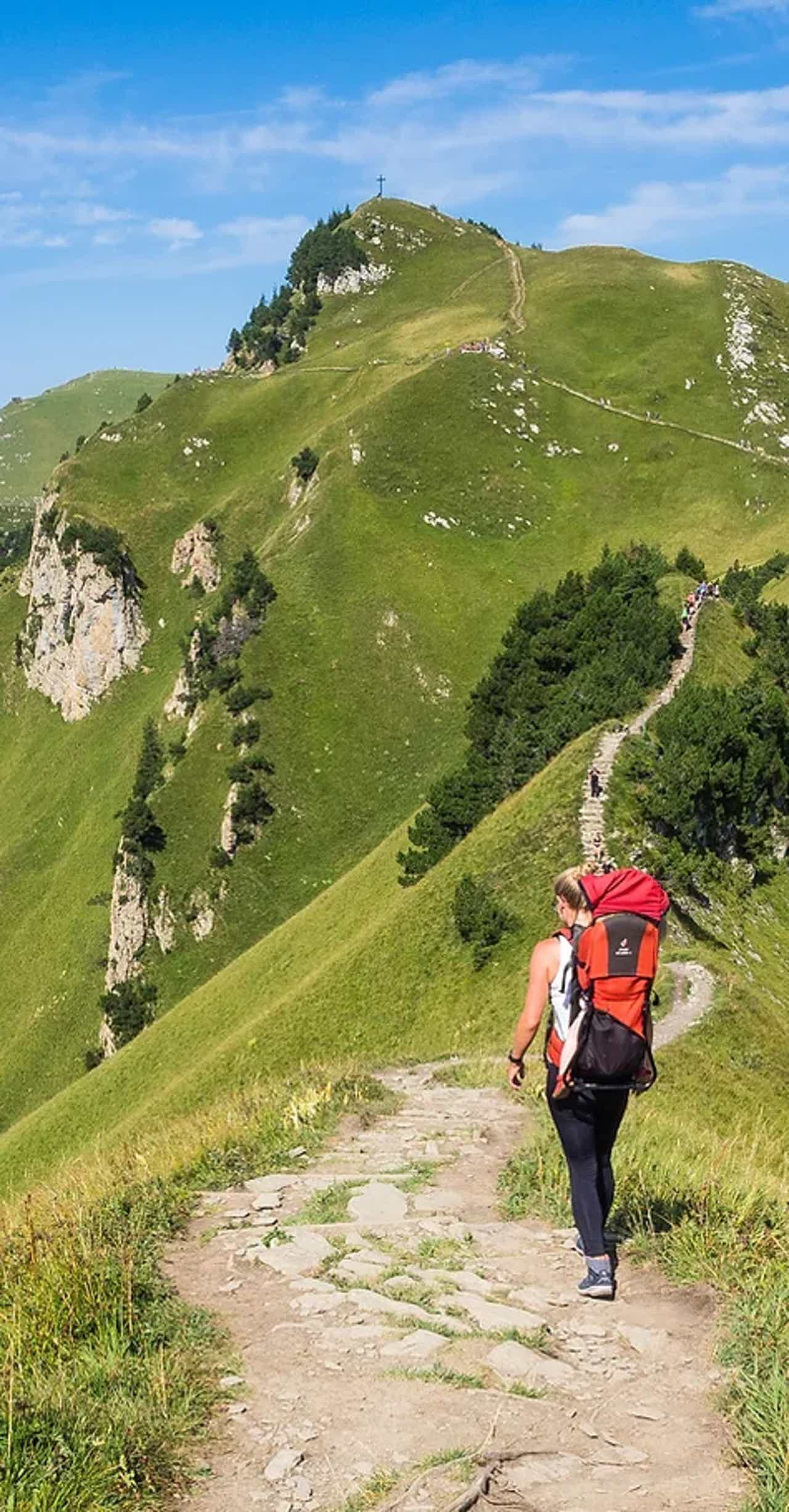 Hiker with red backpack walking on mountain trail on a sunny day.