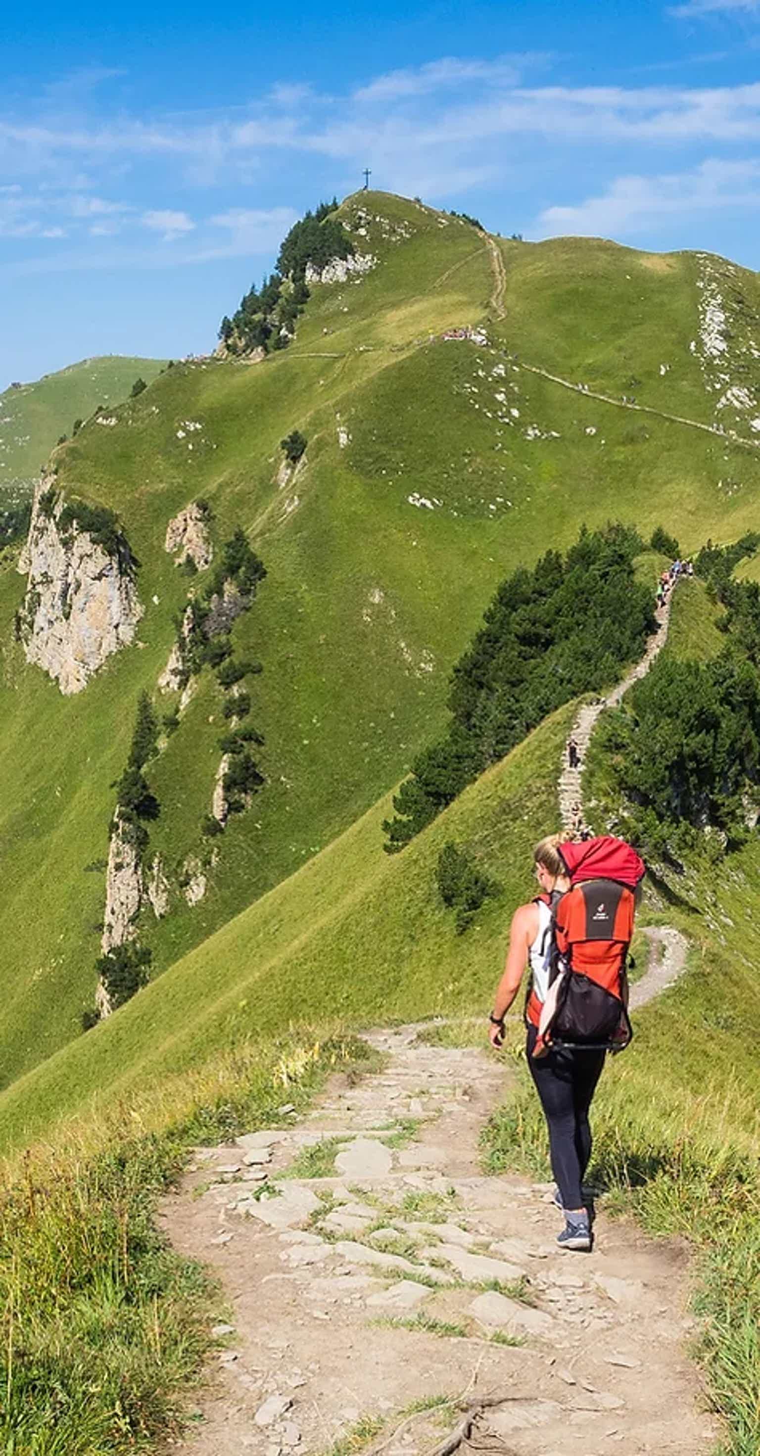 Hiker with red backpack walking on mountain trail on a sunny day.