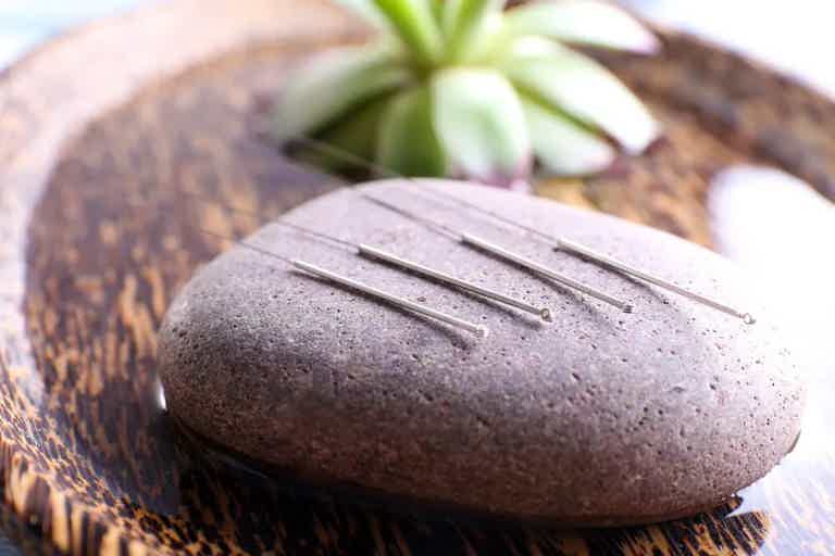 Smooth stone with acupuncture needles on a woven mat, hinting at alternative medicine practices.