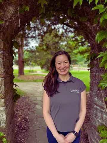 Smiling woman standing on a shaded garden path framed by leafy arching trees
