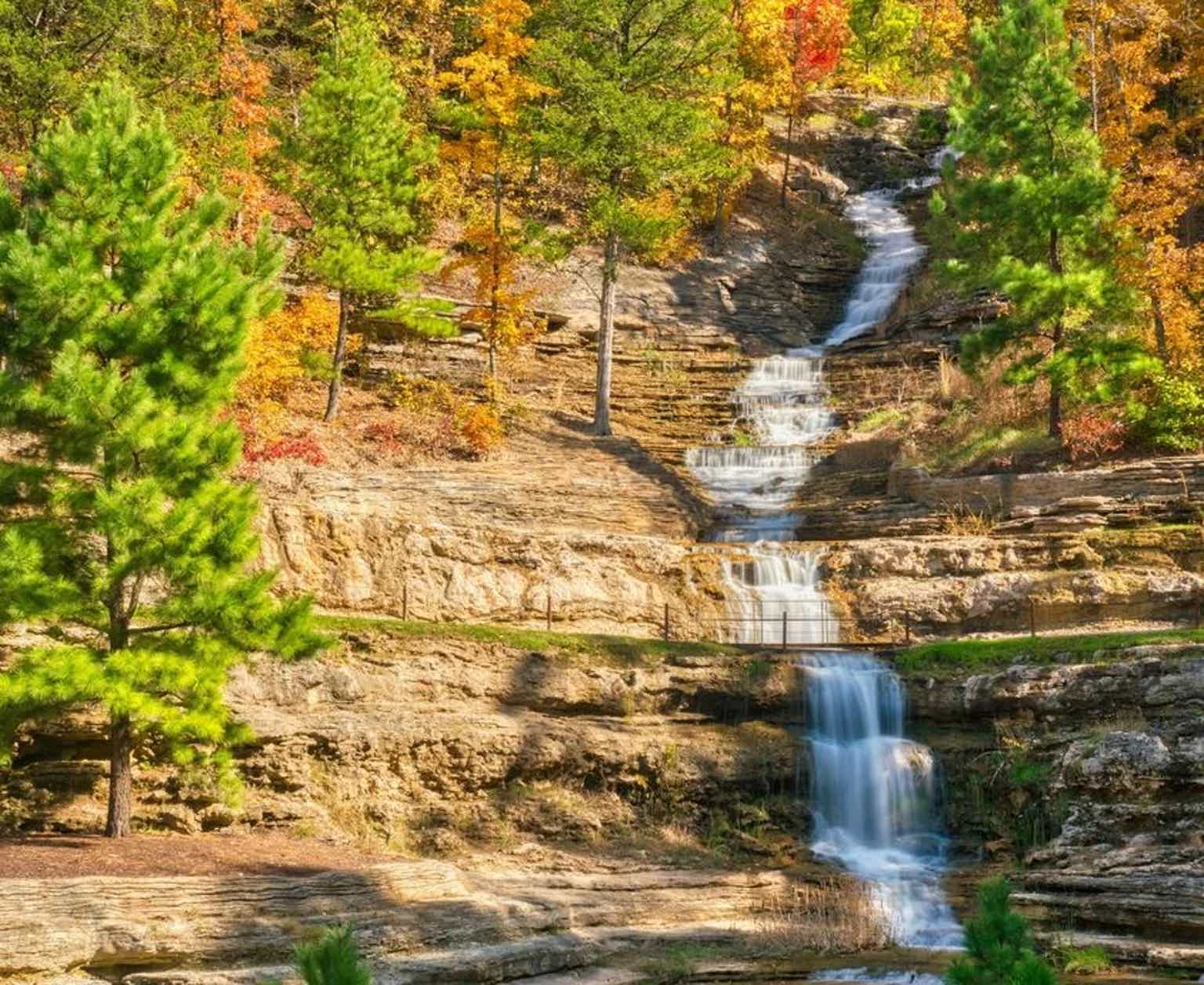 A cascading waterfall amid autumn-colored trees and rocky terrain.