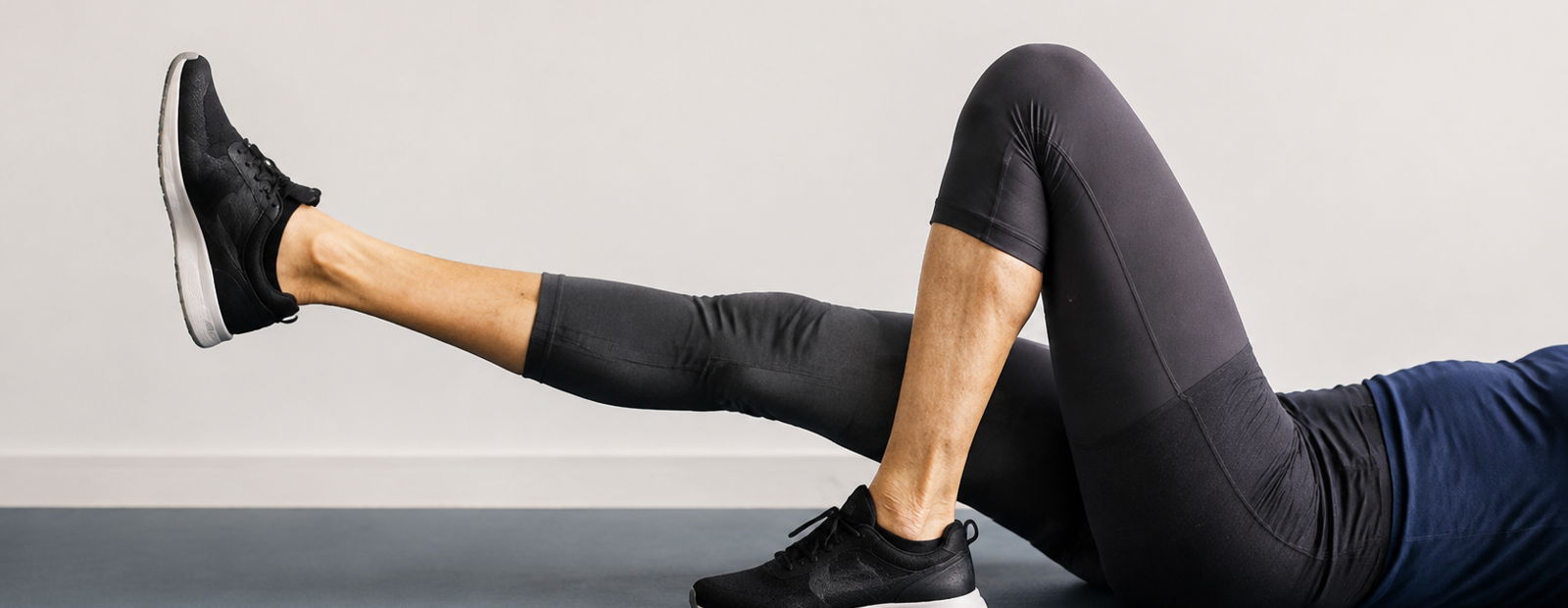 Person performing a glute bridge on a floor, wearing black sneakers and leggings.
