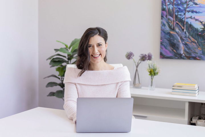 Dr. Andrea Gri, ND, smiling at her desk with a laptop