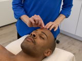 Practitioner in blue places an acupuncture needle as the patient relaxes in a clinic room