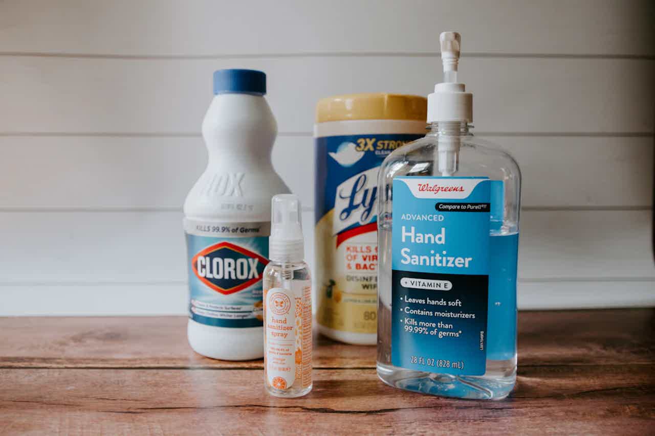 Bottles of cleaning and hand sanitizer on a wooden surface: Clorox, disinfecting wipes, and “Hand Sanitizer.”