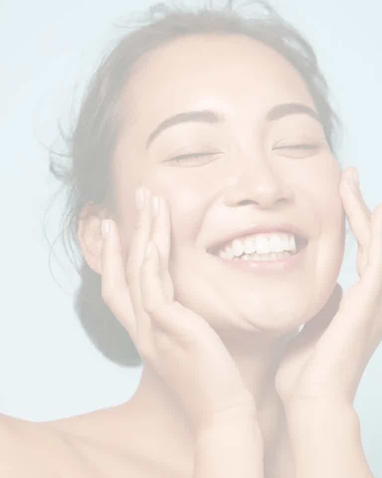 Smiling woman with eyes closed, gently cupping cheeks, conveying happiness and contentment.