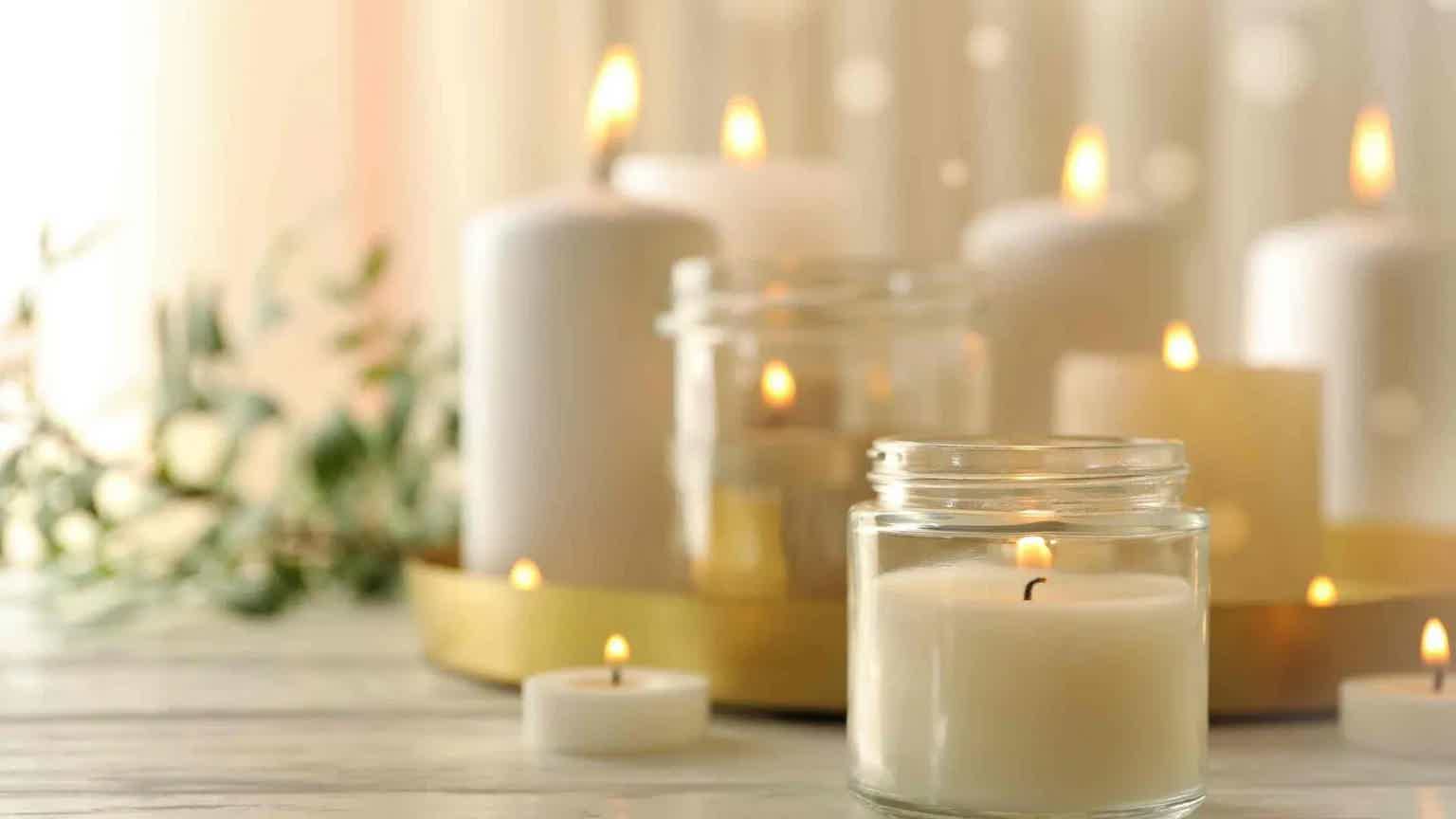Softly lit candles in glass holders and background, warm glow on a stone table with greenery.