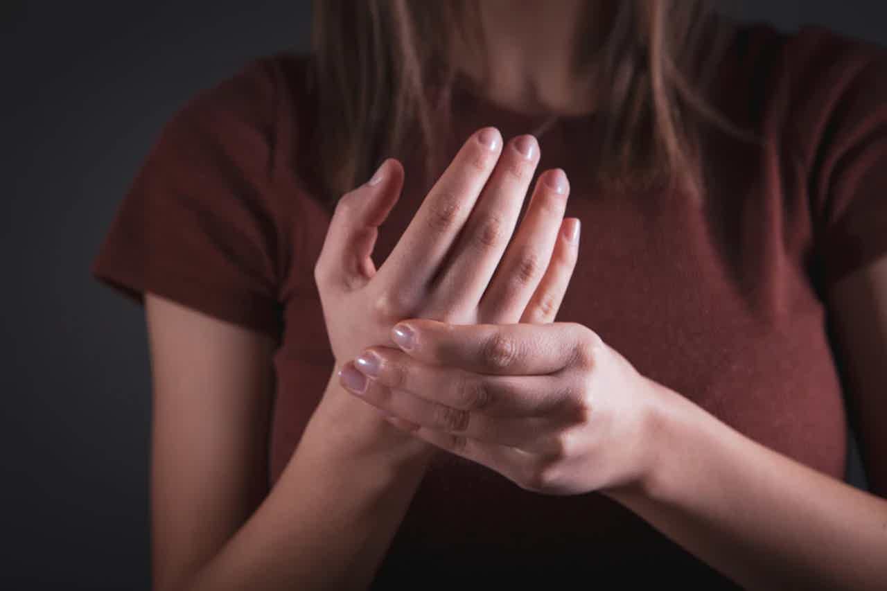 Person covering mouth with hand, fingers extended, wearing short-sleeve maroon shirt; soft indoor lighting.
