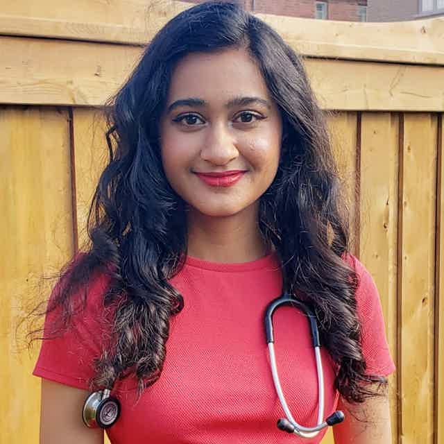 Smiling woman with wavy brown hair sits on brown leather couch, holding a teal mug, in a cozy living room.