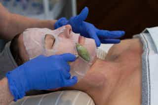Clinician in blue gloves uses a tool to examine and treat a patient’s forearm, applying sterile gauze and dressings.