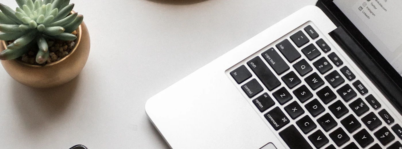 Black iPhone, white laptop, red coffee in glass on cork coaster, and small succulent on light tabletop.