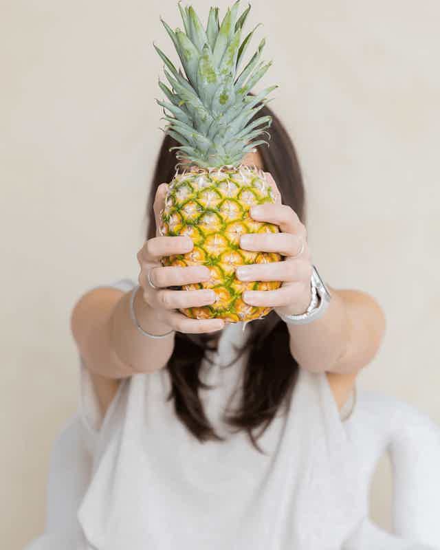Person holding a ripe pineapple with both hands, foreground centered, neutral background.