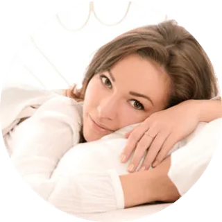 Woman resting her head on a pillow, looking relaxed and content, with a soft-focus background.