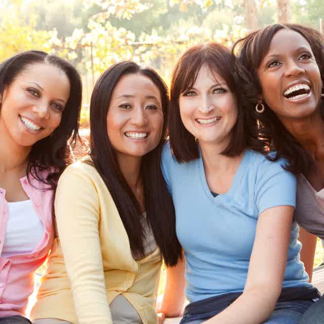 Group of diverse women smiling outdoors, close-up portrait in warm sunlight.