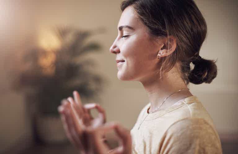 Side profile of a woman with hands raised in meditation, warm light, soft blurred background.