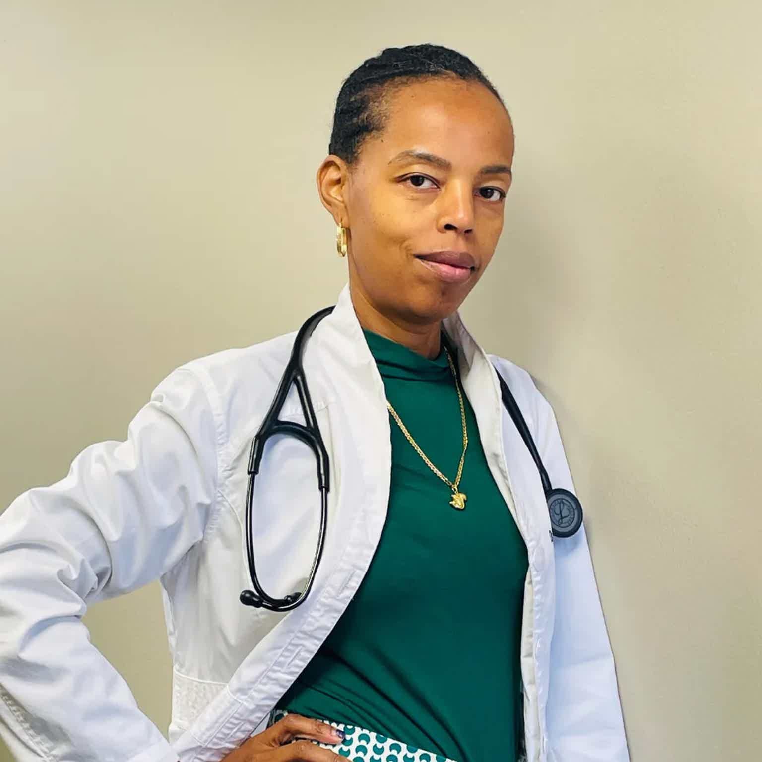 Female doctor wearing green top and white coat with stethoscope, confident pose, indoors.