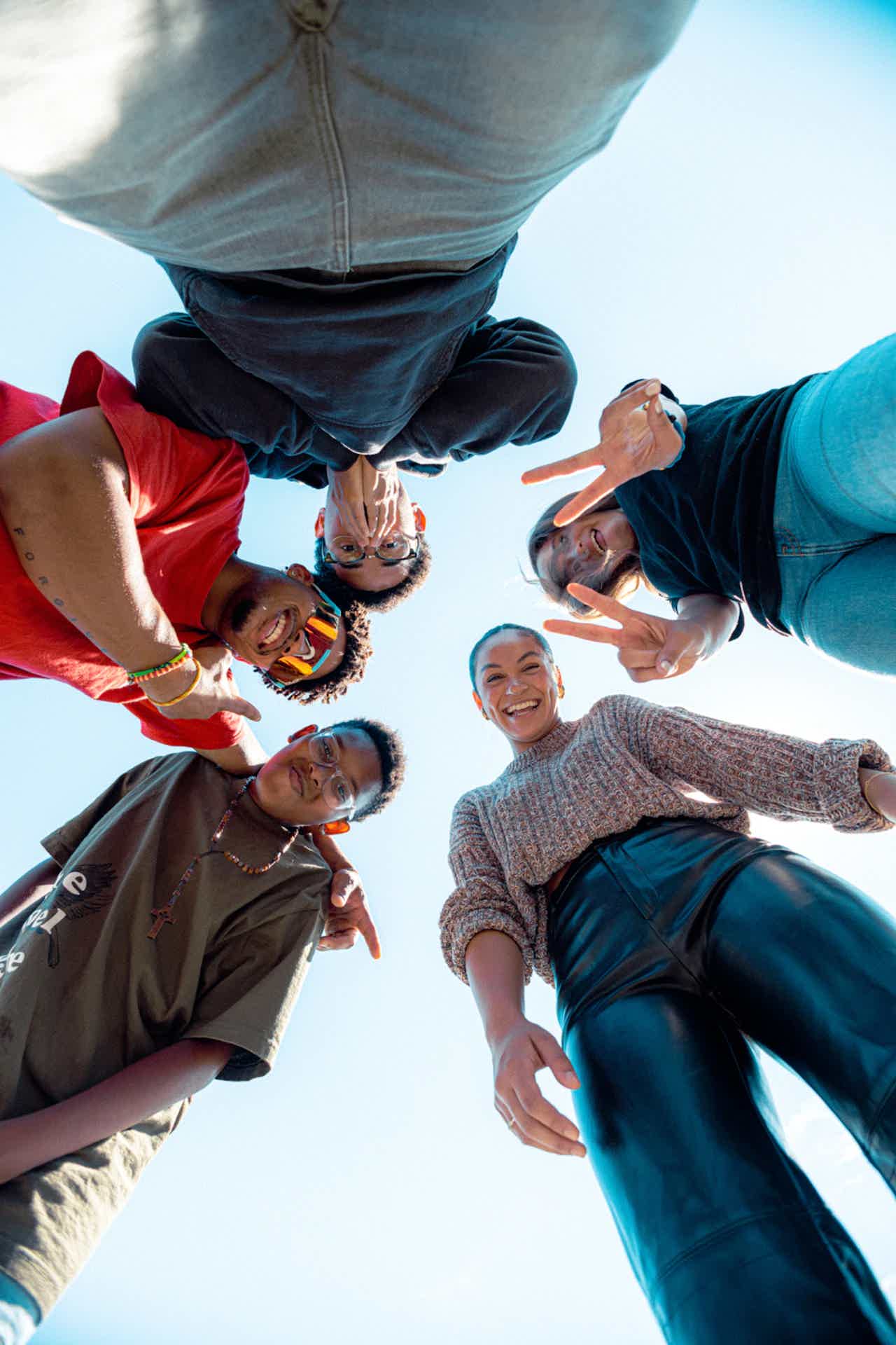 Group of diverse friends standing in a circle, looking down at camera and smiling.