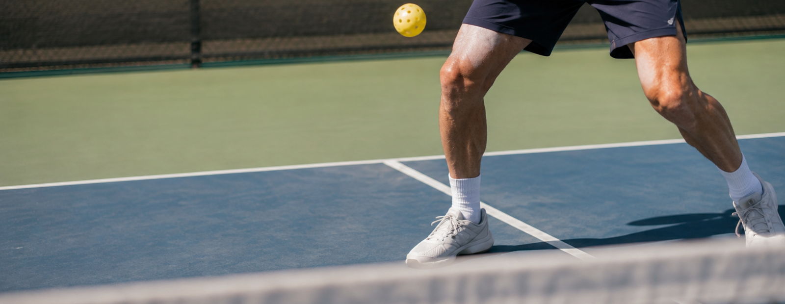 Tennis player mid-sprint on court, preparing to hit a yellow ball over the net.