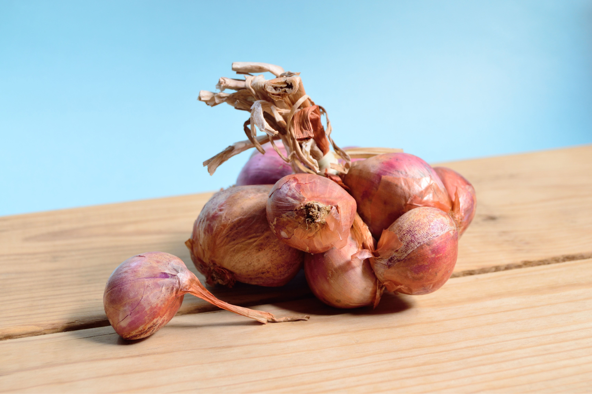 A bunch of fresh shallots, a high-FODMAP food, resting on a wooden surface against a blue background.