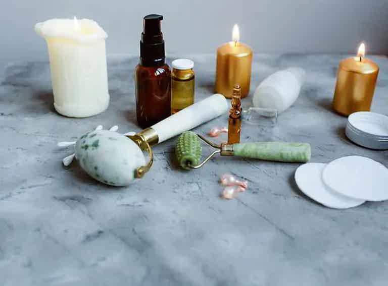 Spa essentials with jade roller, candles, skincare bottles, and cotton pads on a marble surface.