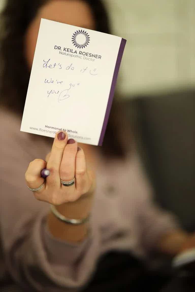 Business card held toward camera, handwritten message visible, blurred person in background.