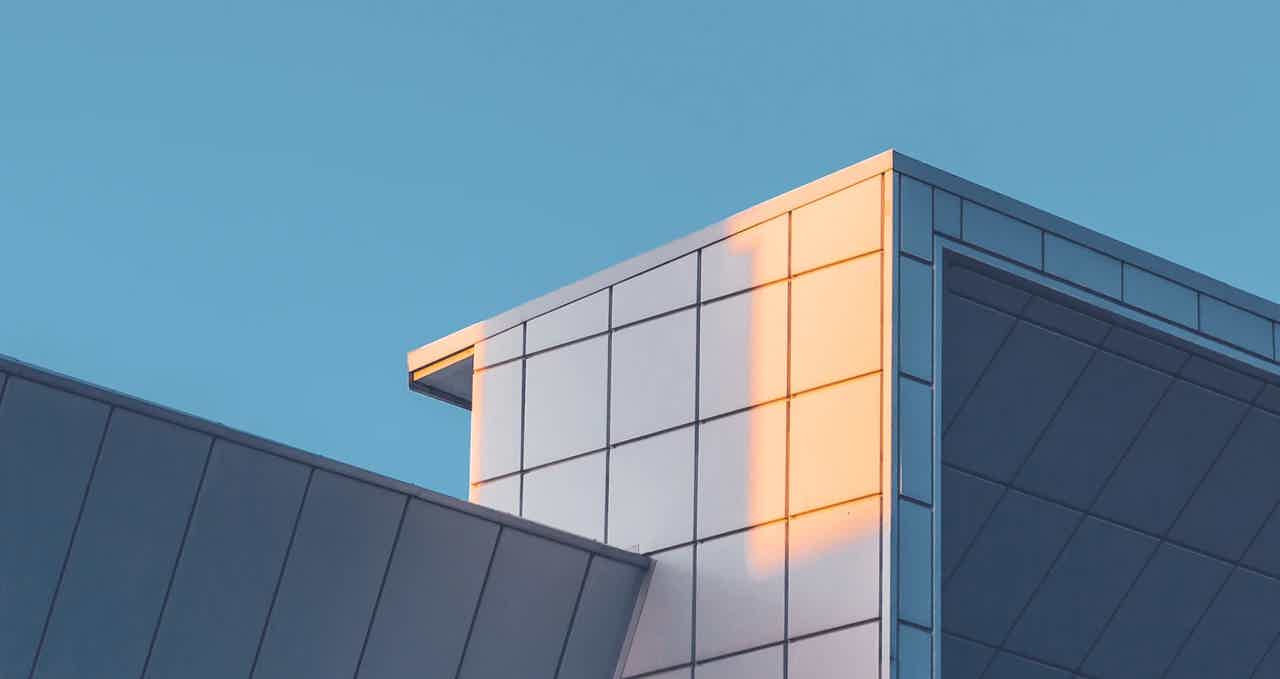 Modern office building corner with glass facade at sunset against a blue sky, warm light reflecting on windows