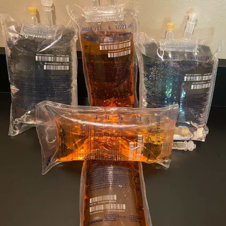 IV bags with colored liquids in clear pouches on a black surface, arranged in a cluster.