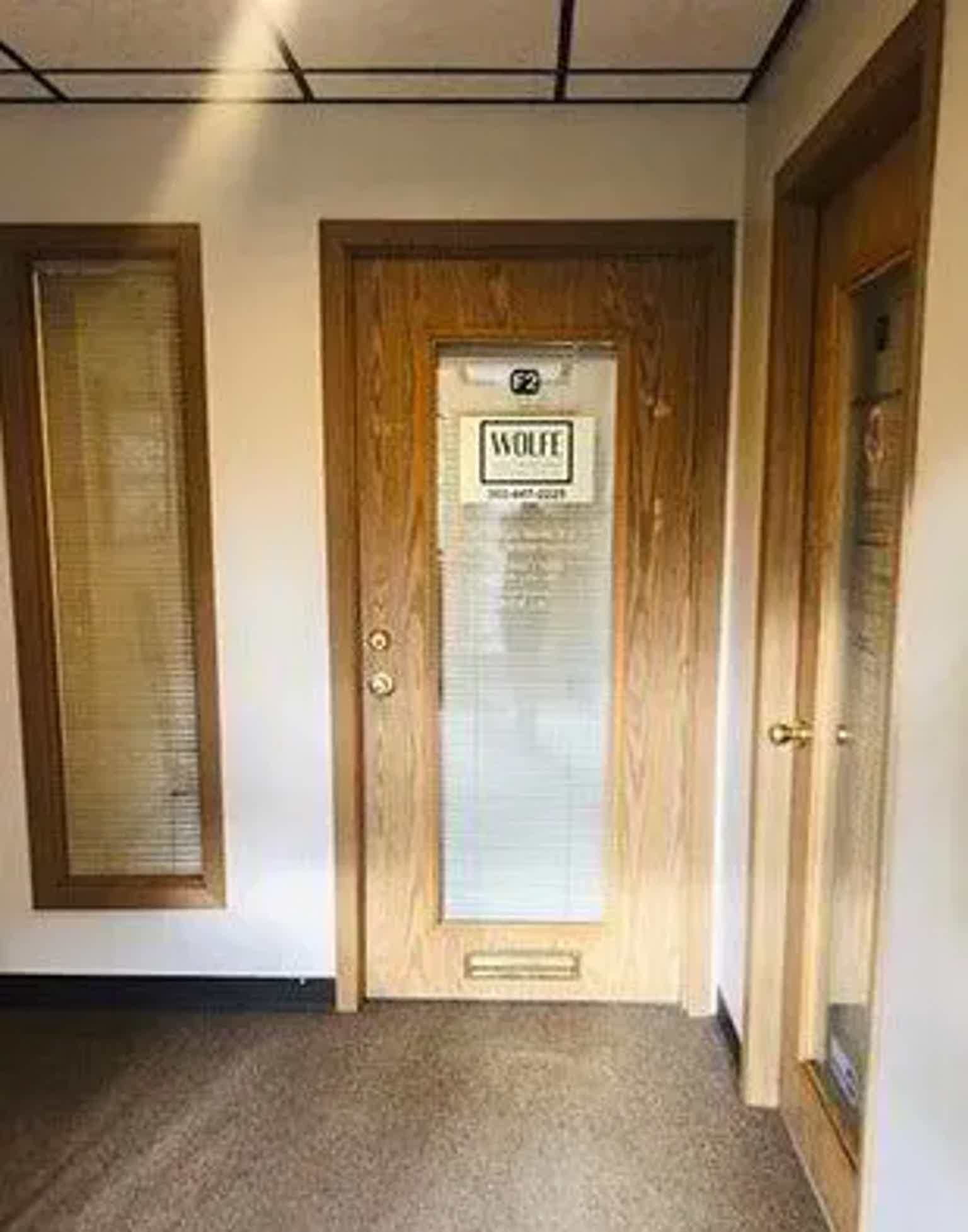 Wood-paneled hallway with glass door labeled “Wolfe” and side doors, brass handles, dim lighting.