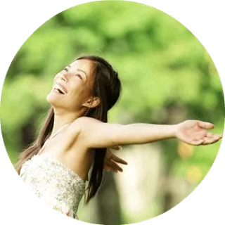 Woman with arms outstretched, laughing in a sunny, green park.