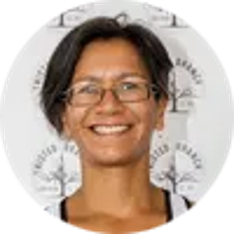 Smiling woman with short dark hair and glasses, framed in a circular logo with subtle tree icons and writing.