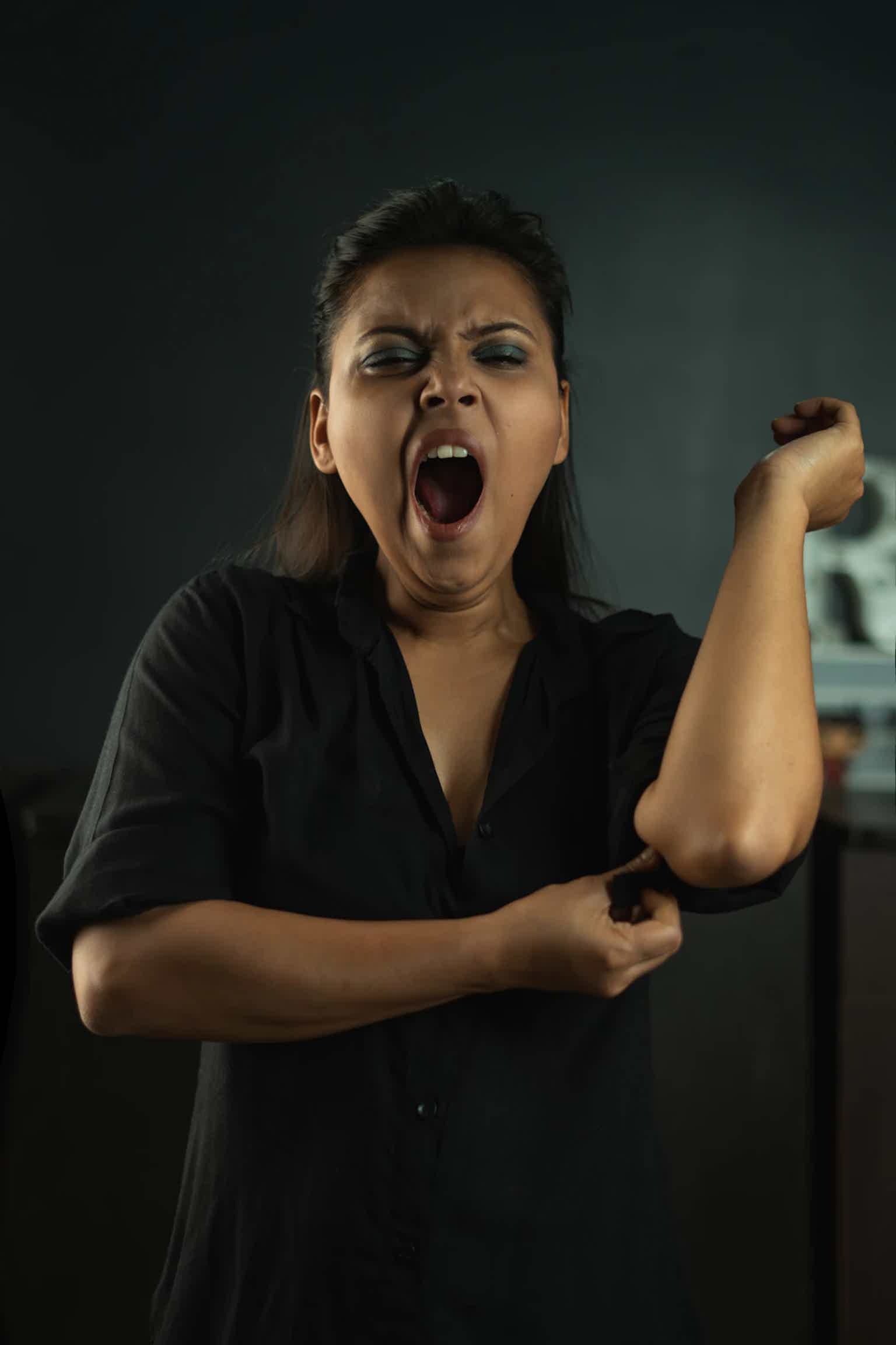 A woman in a black shirt is stretching her arm and shouting with mouth open, eyes closed.