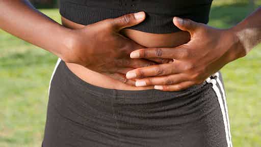 Person in black sportswear clutches their stomach with both hands outdoors on grass.