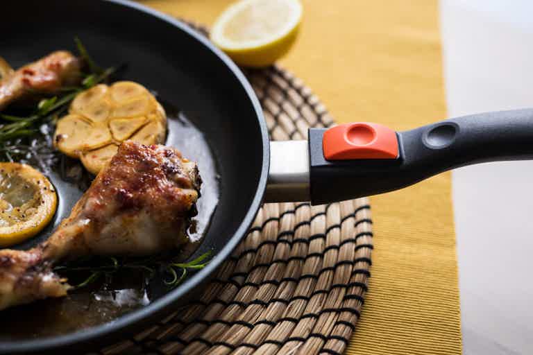Pan-seared chicken leg in a skillet with lemon slices and herbs on a woven placemat.