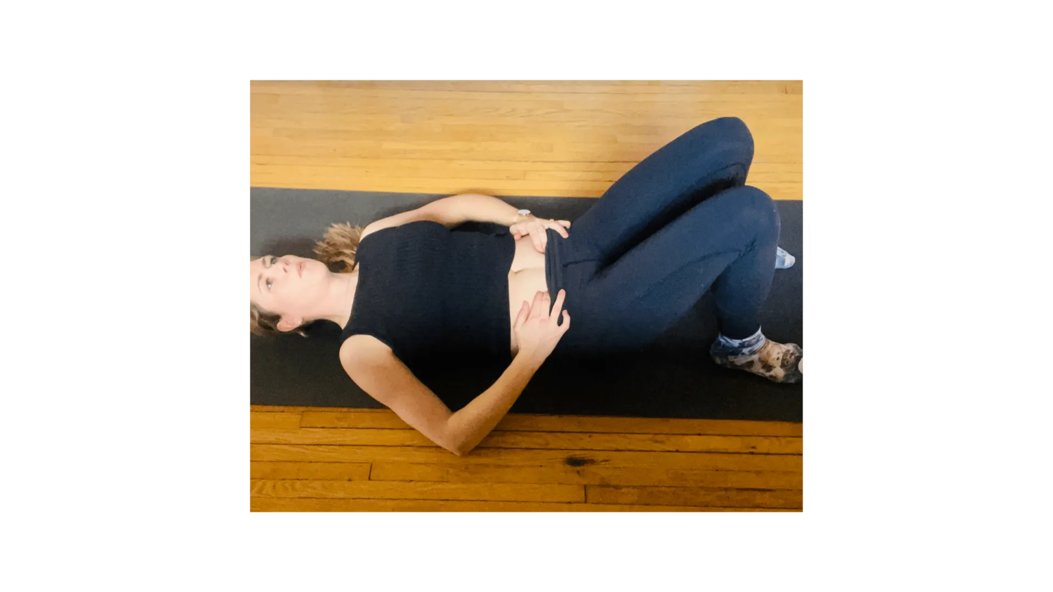 Woman in black leggings lying on a mat performing a stretching pose, legs raised against the wall.
