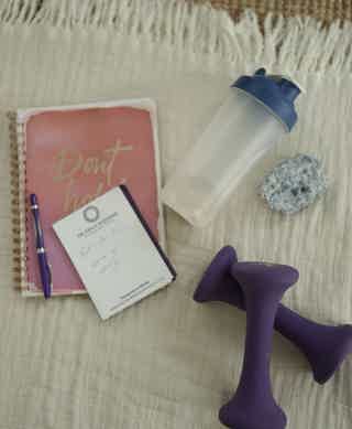 Dumbbells, a reusable shaker bottle, a notebook reading “Don’t quit,” a pen, a small notes card, and a rocky blue stone on a