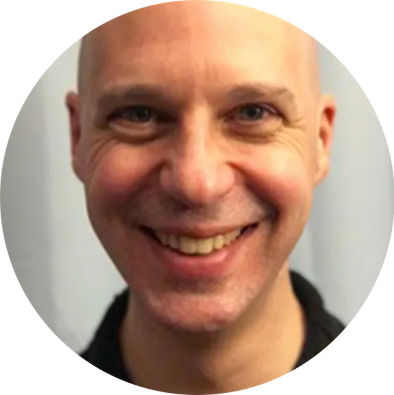 Smiling bald man with blue eyes, close-up headshot against a light background.