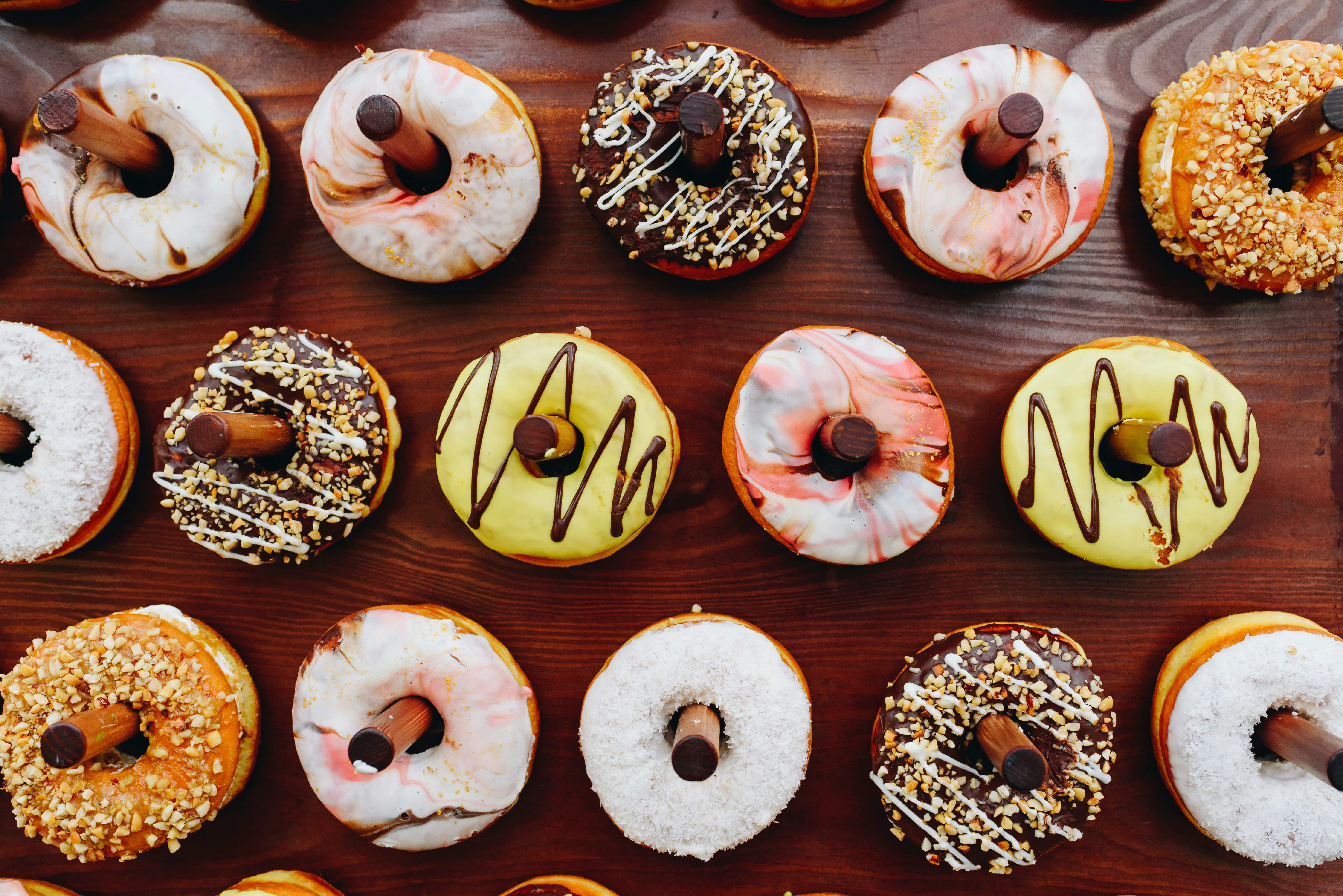 Assorted glazed donuts with chocolate-filled holes, striped frosting, and sprinkles on a wooden table.