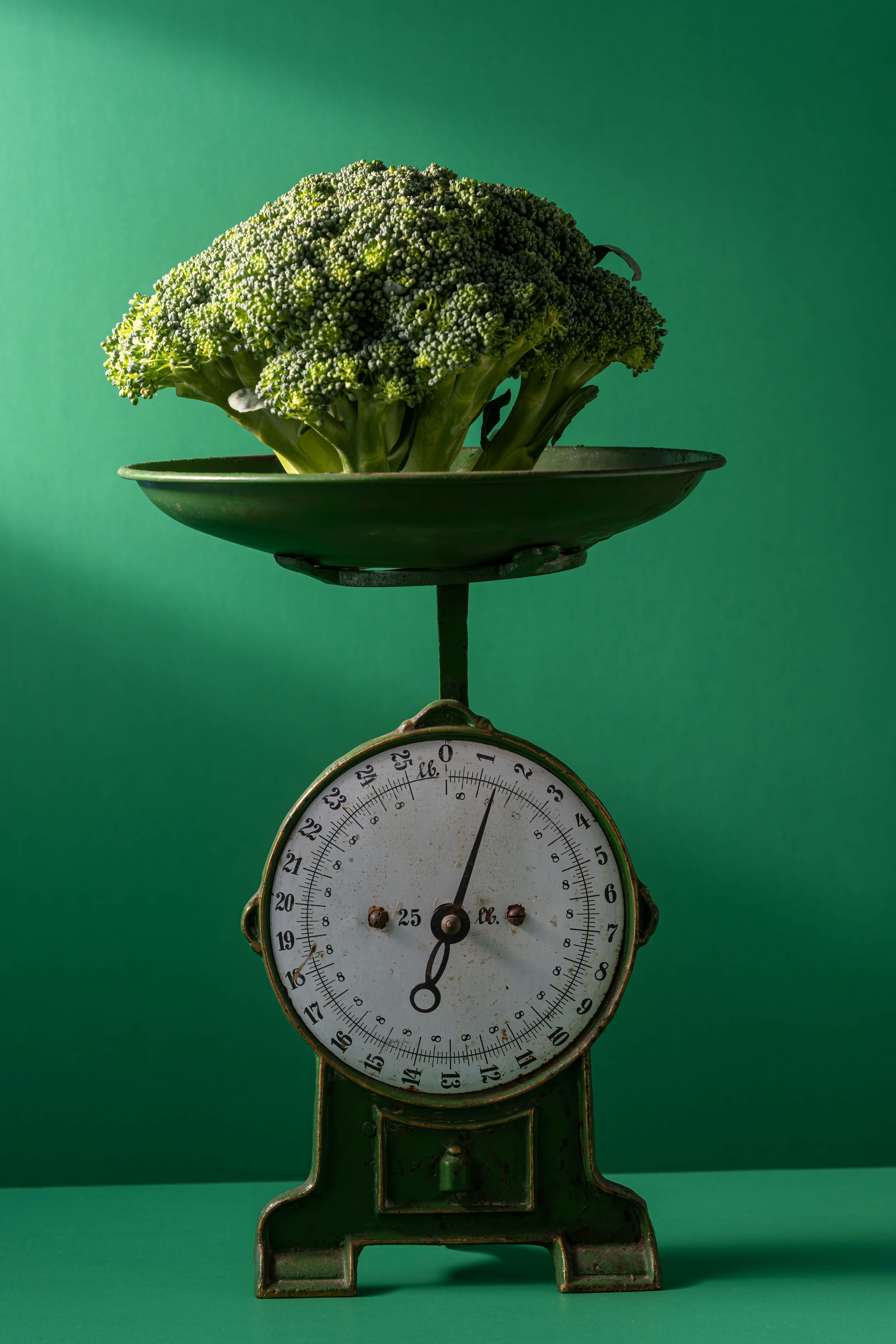 Broccoli head balanced on a vintage scale, against a solid green background