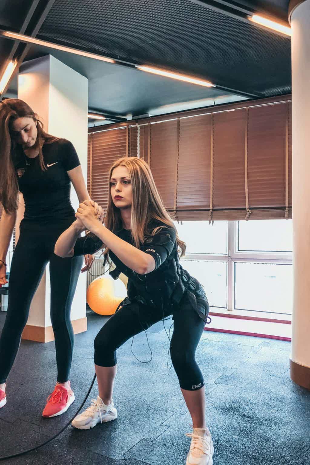 Woman in white blouse with long ponytail standing with arms open in a green forest.