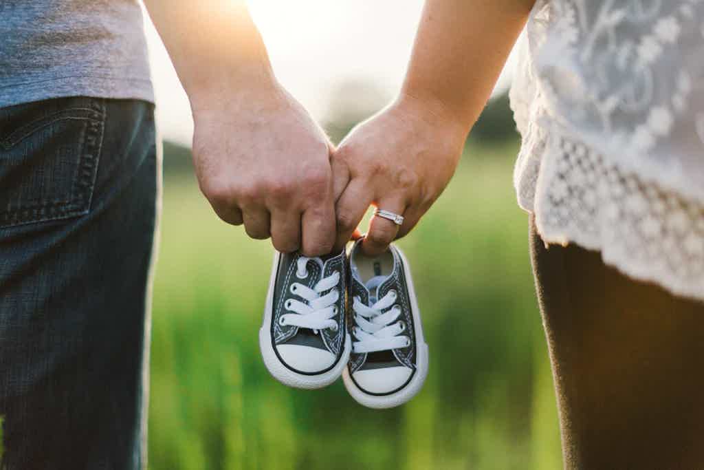 Couple holding small sneakers by laces, sunlight background, tender moment in a field.