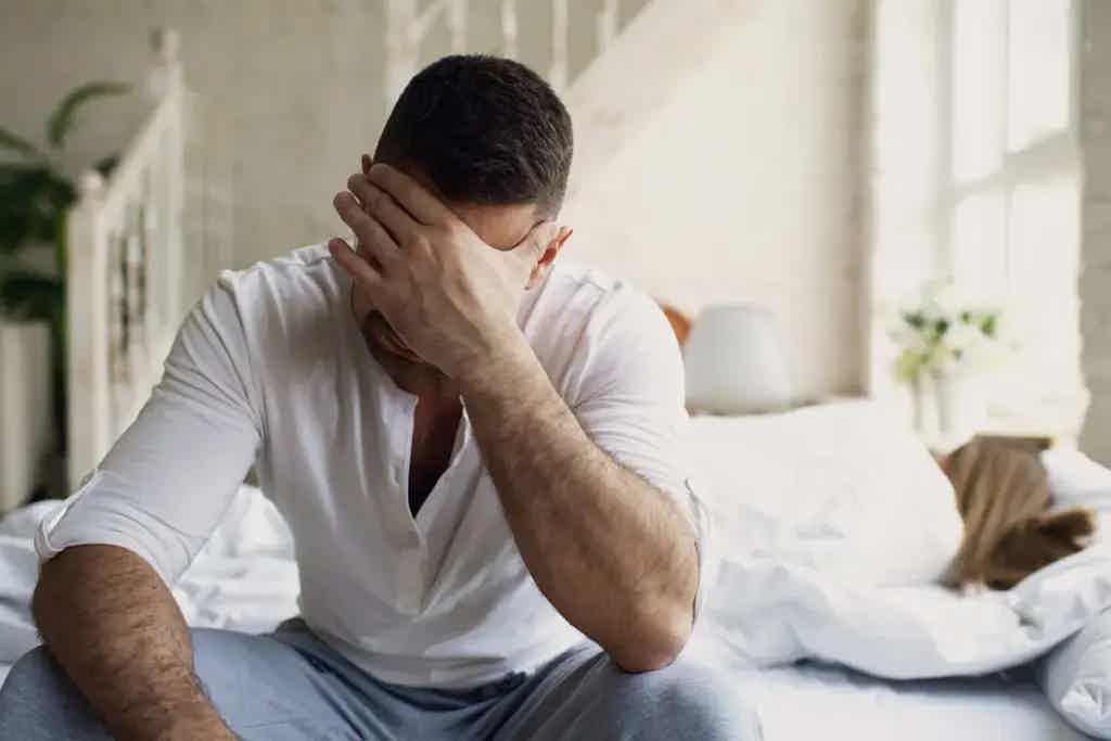 Fatigued man sitting on edge of bed covering his face, showing signs of hormonal imbalance.