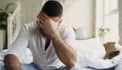 Fatigued man sitting on edge of bed covering his face, showing signs of hormonal imbalance.