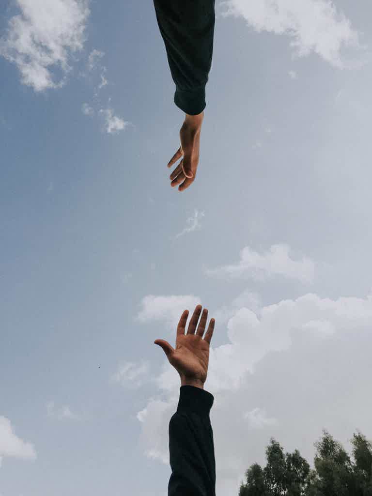 Two hands reaching towards each other against a cloudy sky background.